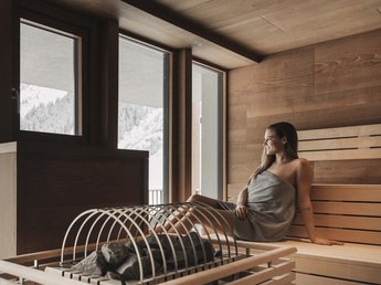 „Nuigkeiten“ aus der Sportalm Frau entspannt in Sauna mit Blick auf schneebedeckte Berge