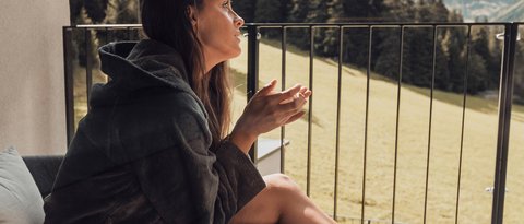 Bilder aus der Sportalm Frau in Bademantel sitzt auf Balkon mit Bergblick am Tisch