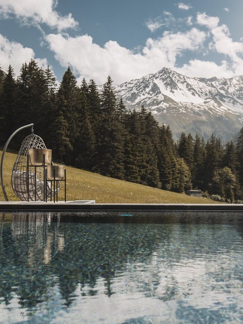 Bilder aus der Sportalm Pool mit Bergblick und hängendem Korbsessel an sonnigem Tag