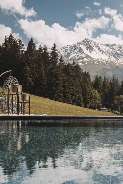 Bilder aus der Sportalm Pool mit Bergblick und hängendem Korbsessel an sonnigem Tag