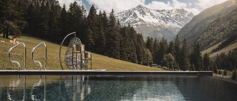 Bilder aus der Sportalm Pool mit Bergblick und hängendem Korbsessel an sonnigem Tag