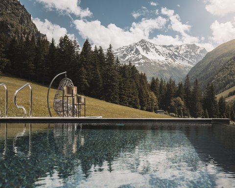 Bilder aus der Sportalm Pool mit Bergblick und hängendem Korbsessel an sonnigem Tag