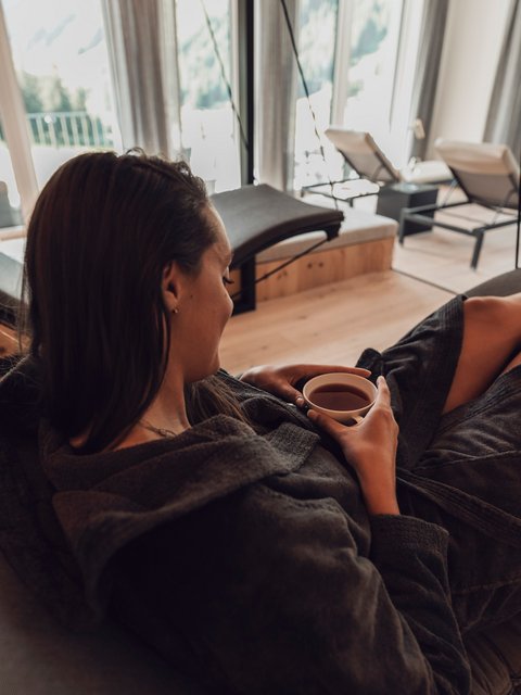 Bilder aus der Sportalm Frau entspannt in Bademantel und trinkt Tee in modernem Spa mit Aussicht