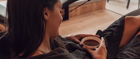 Bilder aus der Sportalm Frau entspannt in Bademantel und trinkt Tee in modernem Spa mit Aussicht