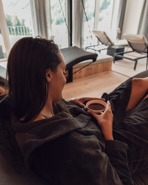 Bilder aus der Sportalm Frau entspannt in Bademantel und trinkt Tee in modernem Spa mit Aussicht