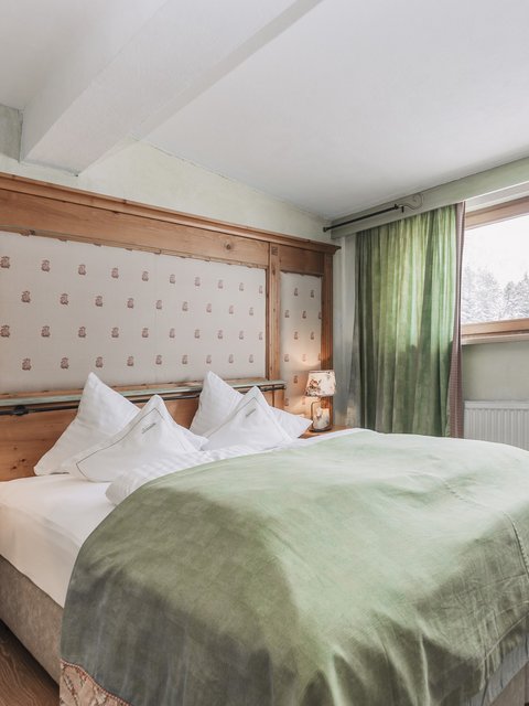 Bilder aus der Sportalm Gemütliches Schlafzimmer mit grünem Bettüberwurf und Holzfenster