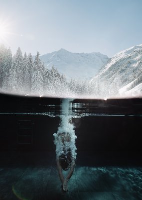Urlaub im Pitztal? Unterkunft mit Pep! Person taucht in Pool mit verschneiten Bergen im Hintergrund