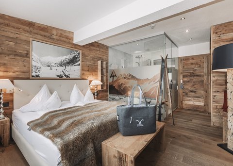 Bilder aus der Sportalm Gemütliches Schlafzimmer mit Holzwänden, Doppelbett und Glasdusche im Hintergrund