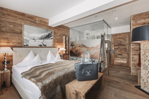 Bilder aus der Sportalm Gemütliches Schlafzimmer mit Holzwänden, Doppelbett und Glasdusche im Hintergrund