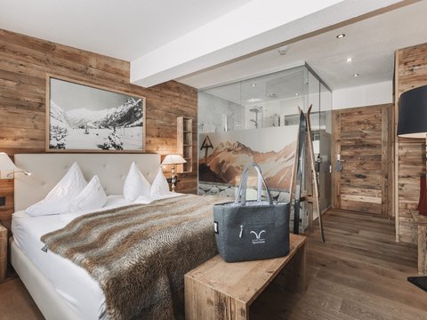 Bilder aus der Sportalm Gemütliches Schlafzimmer mit Holzwänden, Doppelbett und Glasdusche im Hintergrund