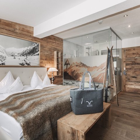 Bilder aus der Sportalm Gemütliches Schlafzimmer mit Holzwänden, Doppelbett und Glasdusche im Hintergrund