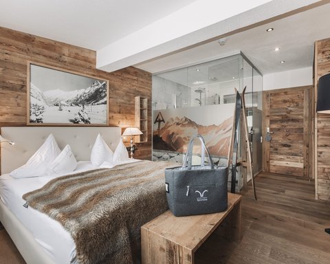 Pictures from Sportalm Cozy bedroom with wooden walls, double bed, and glass shower in the background