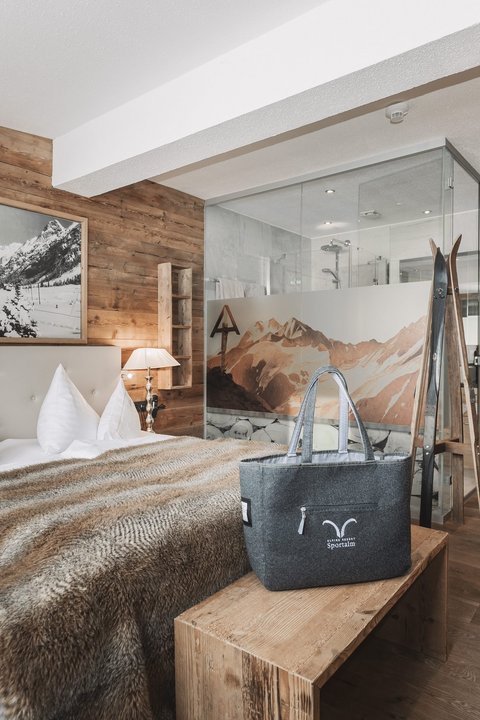 Bilder aus der Sportalm Gemütliches Schlafzimmer mit Holzwänden, Doppelbett und Glasdusche im Hintergrund