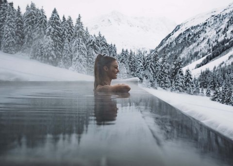 Bilder aus der Sportalm Frau entspannt in beheiztem Außenpool mit verschneiten Bergen im Hintergrund