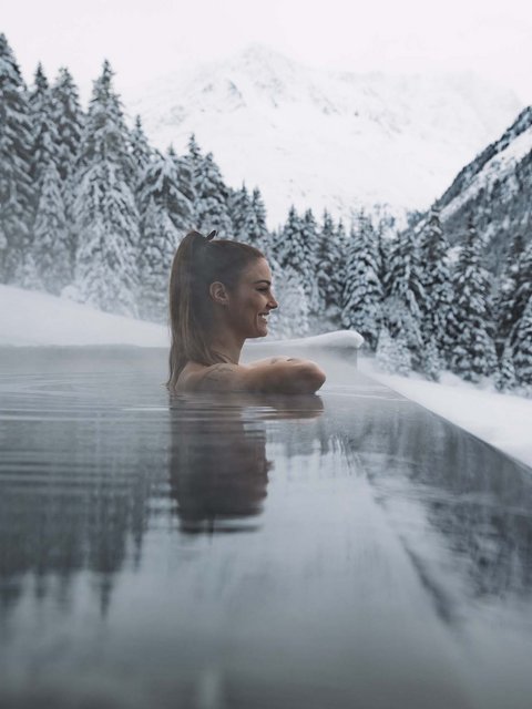Bilder aus der Sportalm Frau entspannt in beheiztem Außenpool mit verschneiten Bergen im Hintergrund