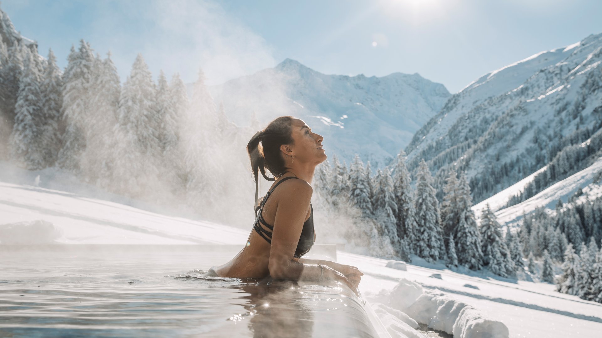 Woman relaxing in outdoor hot tub with snowy mountains in the background
