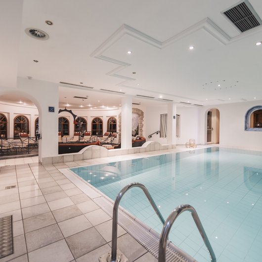 Familienurlab im Wellnessresort in Tirol Innenaufnahme eines hellen Schwimmbads mit Liegestühlen im Hintergrund