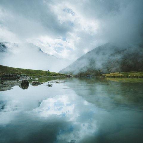 Bilder aus der Sportalm Bergsee mit Reflexion und Nebel an einem bewölkten Tag