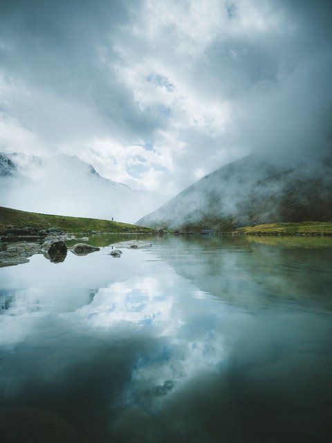 Bilder aus der Sportalm Bergsee mit Reflexion und Nebel an einem bewölkten Tag
