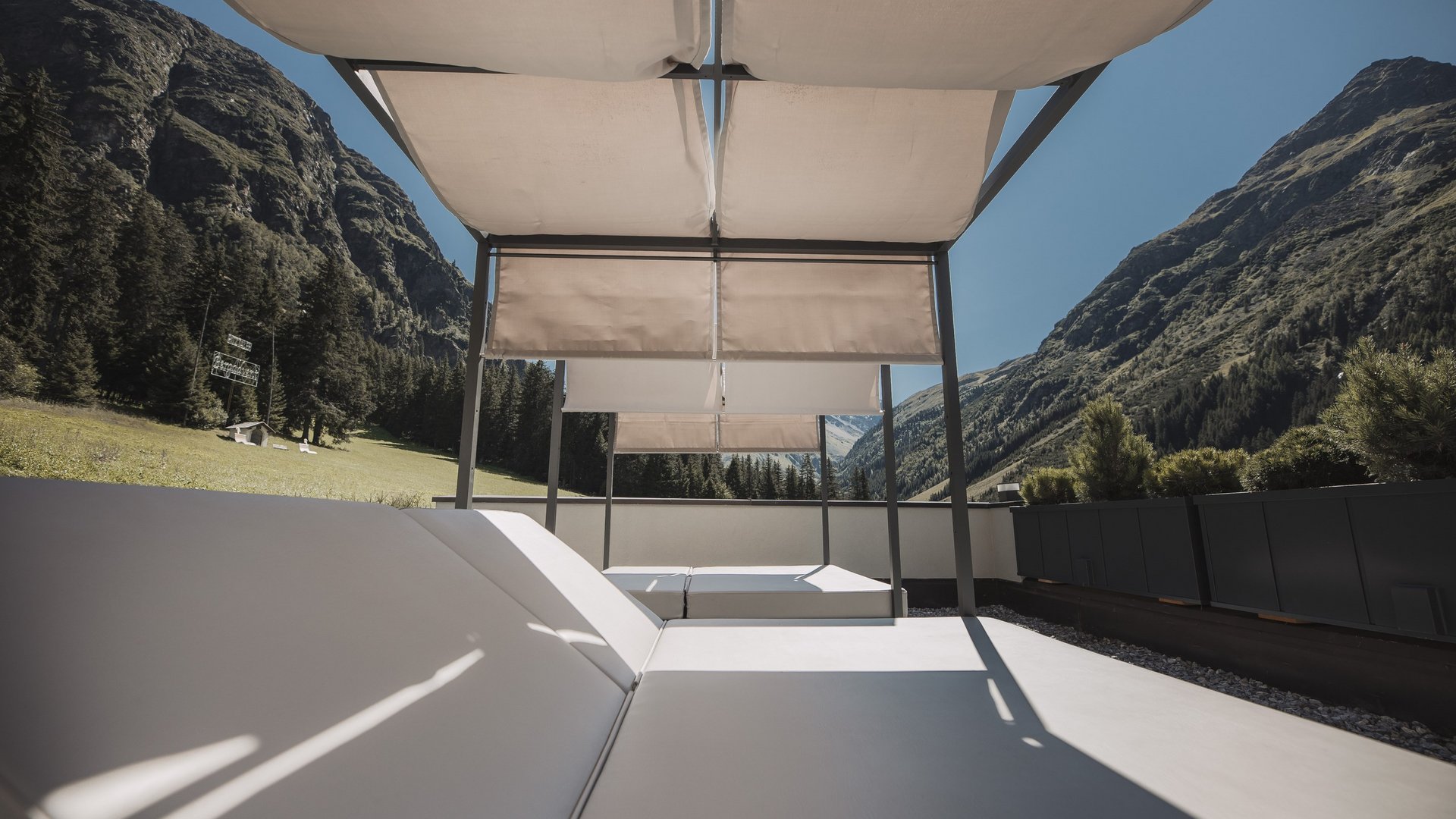 Urlaub im Pitztal? Unterkunft mit Pep! Liegestühle mit Sonnenschutz auf Terrasse vor Berglandschaft bei klarem Himmel