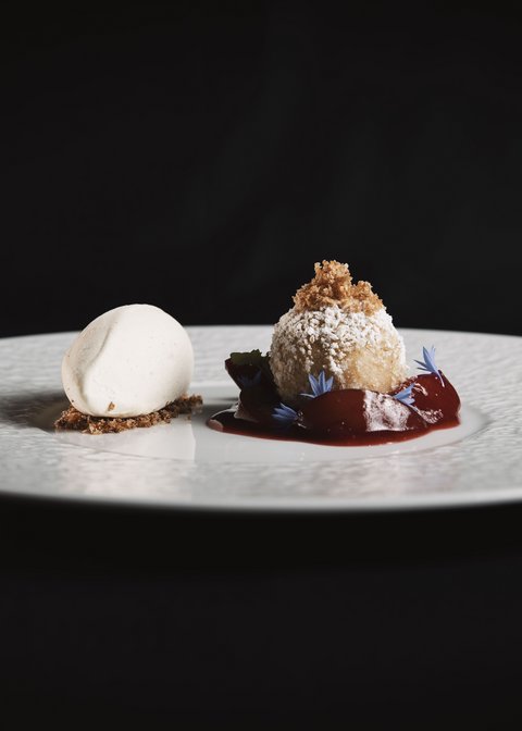 Bilder aus der Sportalm Feines Dessert mit hellem Eis und Kugel mit Puderzucker und roter Sauce