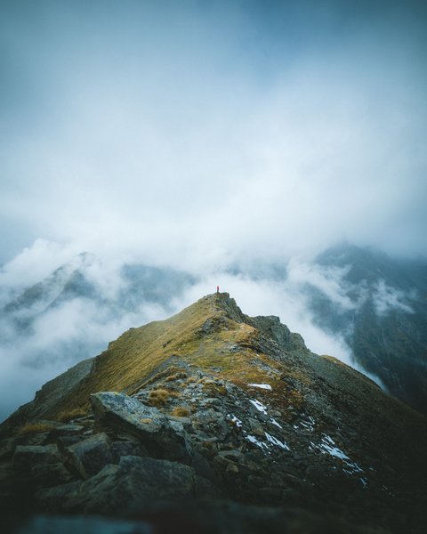 Bilder aus der Sportalm Person steht auf Berggipfel umgeben von Nebel und Wolken