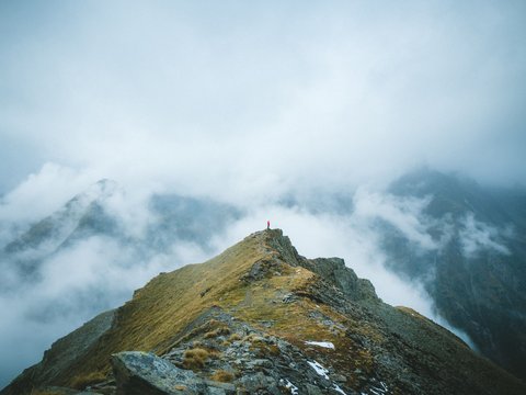 Bilder aus der Sportalm Person steht auf Berggipfel umgeben von Nebel und Wolken