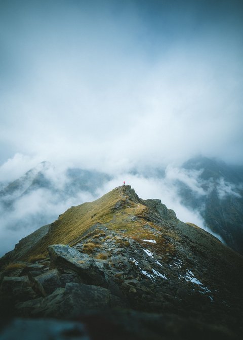 Bilder aus der Sportalm Person steht auf Berggipfel umgeben von Nebel und Wolken