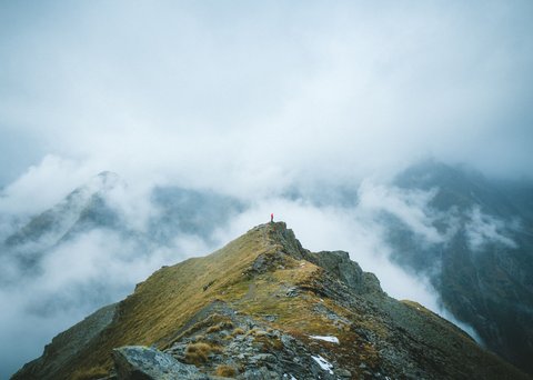 Bilder aus der Sportalm Person steht auf Berggipfel umgeben von Nebel und Wolken