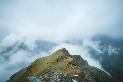 Pictures from Sportalm Person standing on mountain peak surrounded by fog and clouds