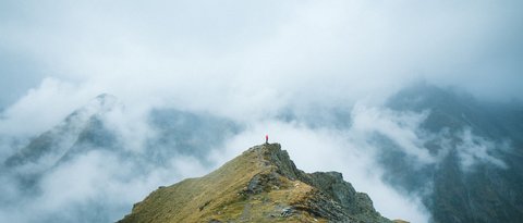 Bilder aus der Sportalm Person steht auf Berggipfel umgeben von Nebel und Wolken