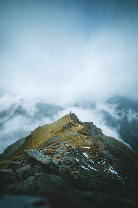 Pictures from Sportalm Person standing on mountain peak surrounded by fog and clouds