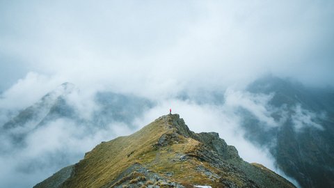 Bilder aus der Sportalm Person steht auf Berggipfel umgeben von Nebel und Wolken