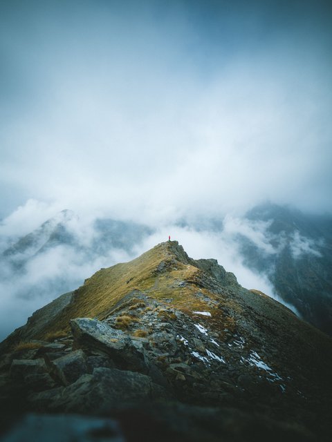 Pictures from Sportalm Person standing on mountain peak surrounded by fog and clouds