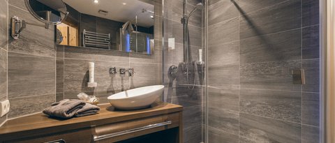 Bilder aus der Sportalm Modernes Badezimmer mit grauen Fliesen, Holzunterschrank und Glasdusche