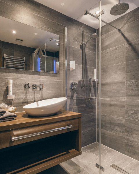 Bilder aus der Sportalm Modernes Badezimmer mit grauen Fliesen, Holzunterschrank und Glasdusche