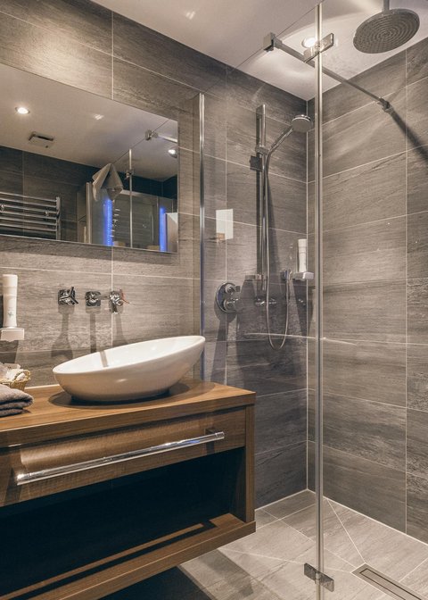 Bilder aus der Sportalm Modernes Badezimmer mit grauen Fliesen, Holzunterschrank und Glasdusche