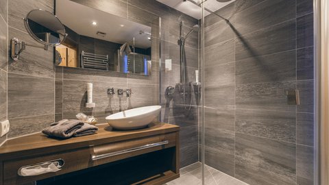 Bilder aus der Sportalm Modernes Badezimmer mit grauen Fliesen, Holzunterschrank und Glasdusche