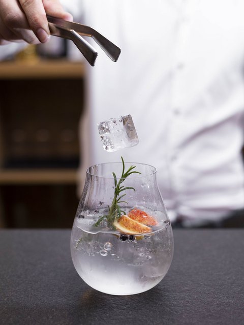 Bilder aus der Sportalm Eiswürfel wird mit einer Zange in ein mit Kräutern und Früchten dekoriertes Getränk gelegt