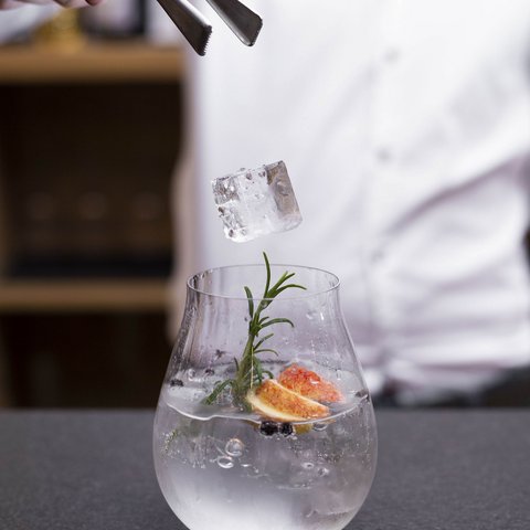 Bilder aus der Sportalm Eiswürfel wird mit einer Zange in ein mit Kräutern und Früchten dekoriertes Getränk gelegt