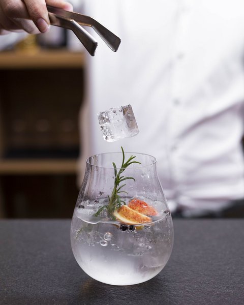 Bilder aus der Sportalm Eiswürfel wird mit einer Zange in ein mit Kräutern und Früchten dekoriertes Getränk gelegt