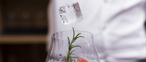 Bilder aus der Sportalm Eiswürfel wird mit einer Zange in ein mit Kräutern und Früchten dekoriertes Getränk gelegt