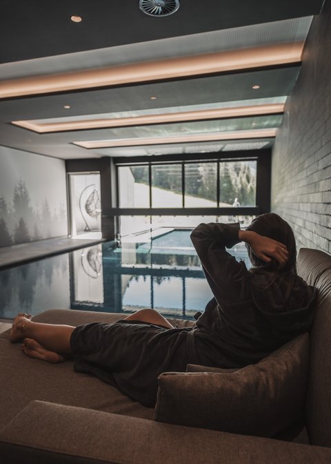 Cosy rooms in Pitztal Woman in bathrobe relaxing on sofa next to indoor pool with view