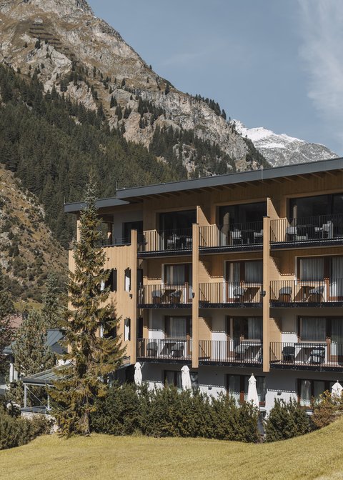 Bilder aus der Sportalm Hotel mit Balkonen vor bewaldetem Berghang und Schnee auf Gipfeln