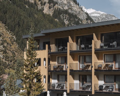 Bilder aus der Sportalm Hotel mit Balkonen vor bewaldetem Berghang und Schnee auf Gipfeln