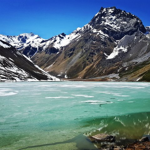 Bilder aus der Sportalm Gefrorener Bergsee mit schneebedeckten Gipfeln unter klarem blauem Himmel