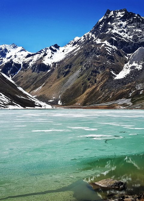 Bilder aus der Sportalm Gefrorener Bergsee mit schneebedeckten Gipfeln unter klarem blauem Himmel