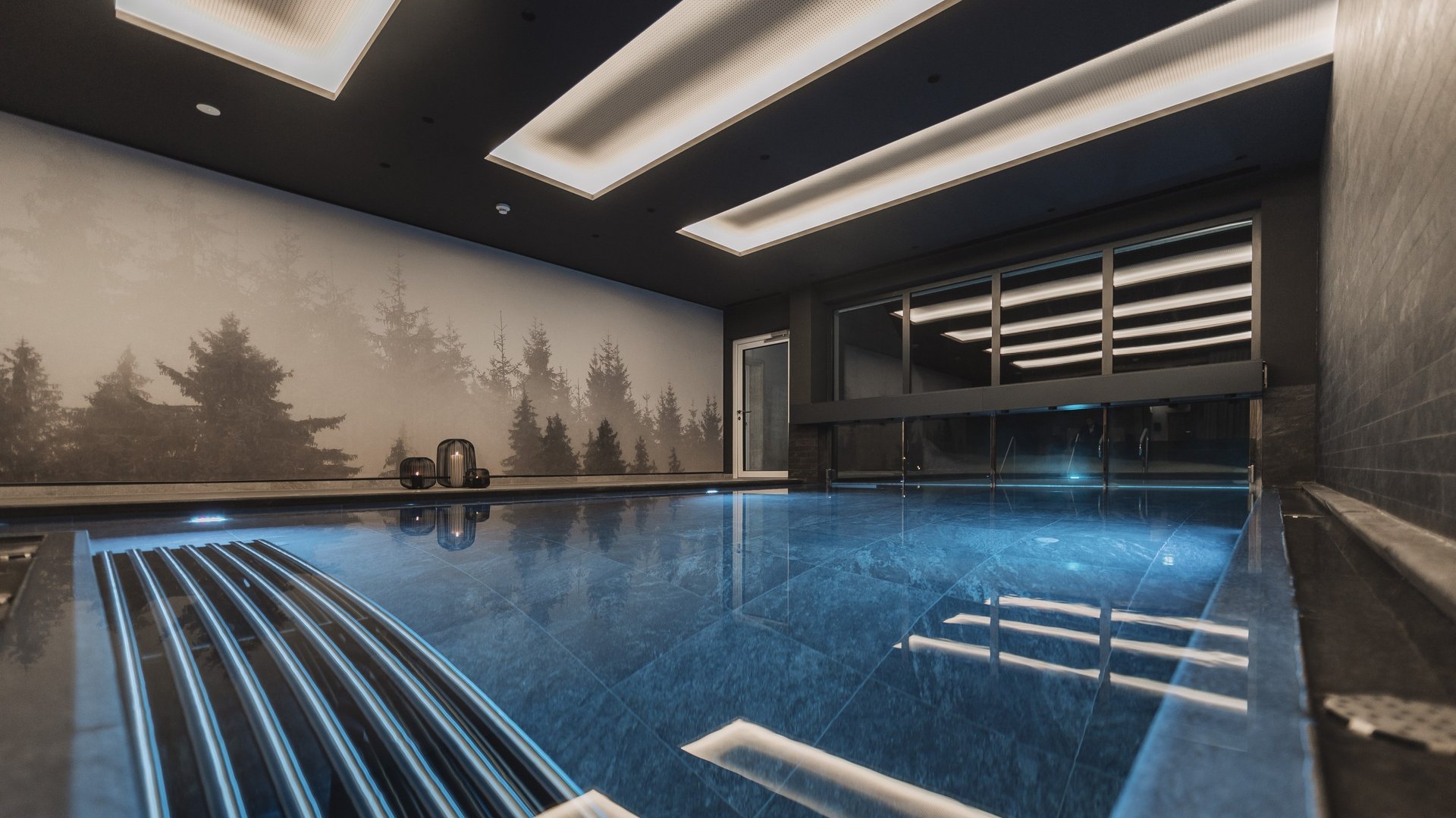 Urlaub im Pitztal? Unterkunft mit Pep! Modernes Innenhallenbad mit blau beleuchtetem Wasser und Waldbild an der Wand