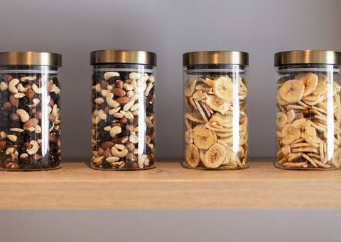 Bilder aus der Sportalm Vier Gläser mit Nüssen und Bananenchips auf einem Holzregal
