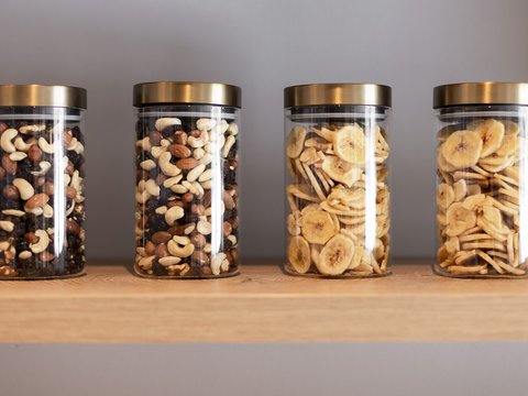 Bilder aus der Sportalm Vier Gläser mit Nüssen und Bananenchips auf einem Holzregal
